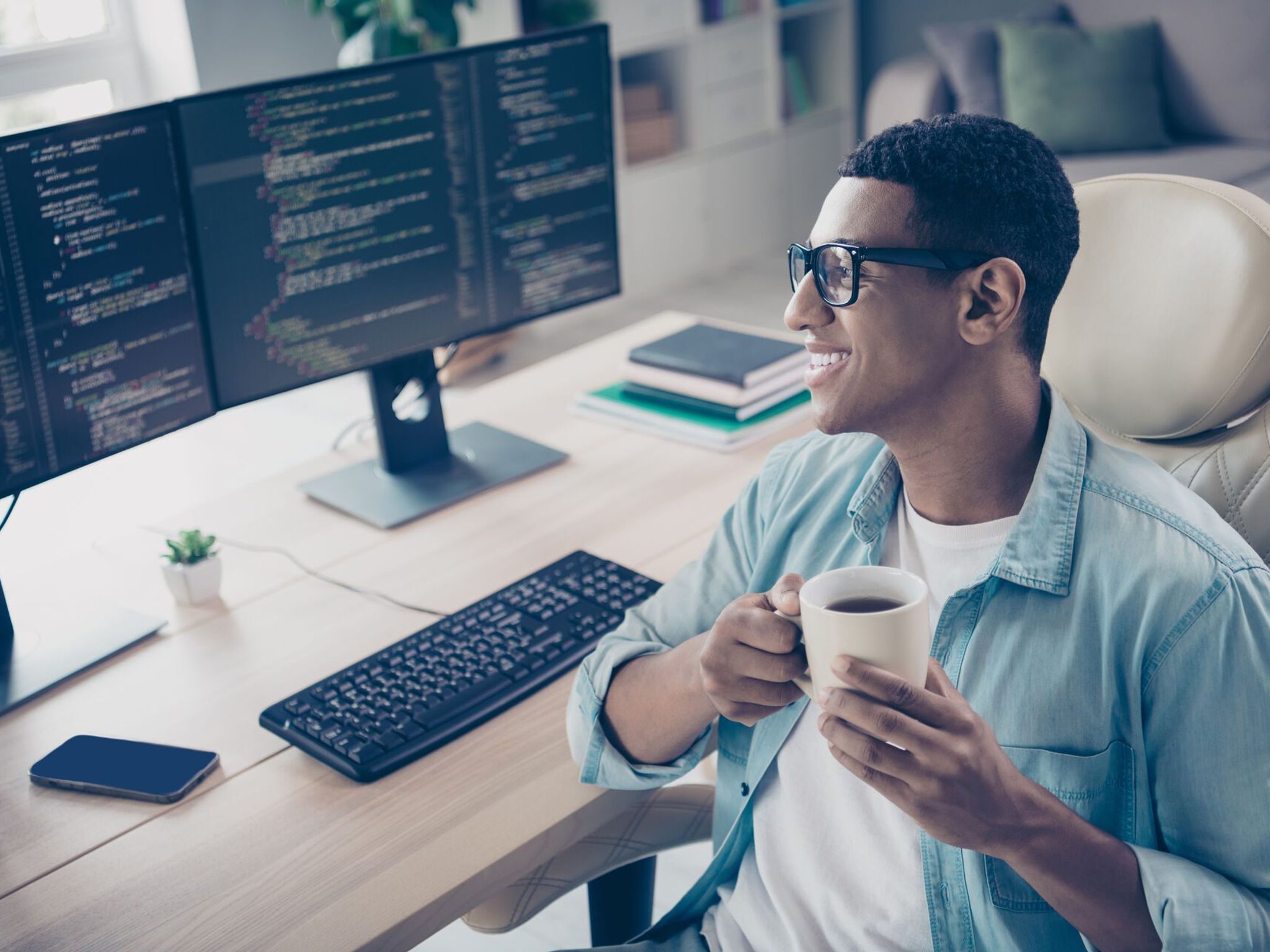A man sitting in front off two monitors with lines of code, smiling